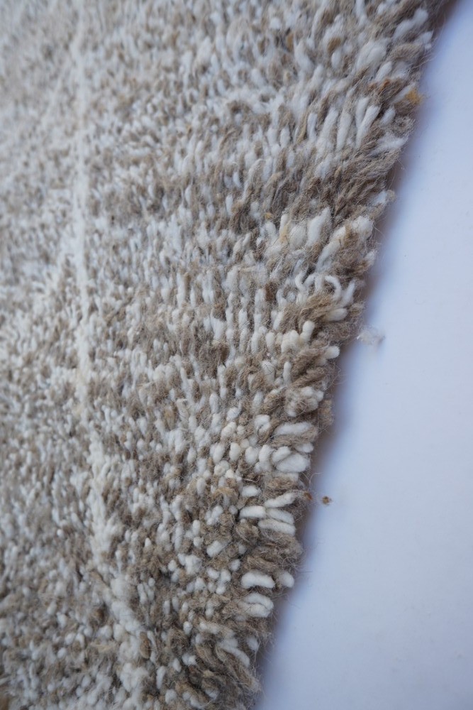 Tapis berbère en laine beige et blanc, avec un design texturé et des motifs géométriques subtils.