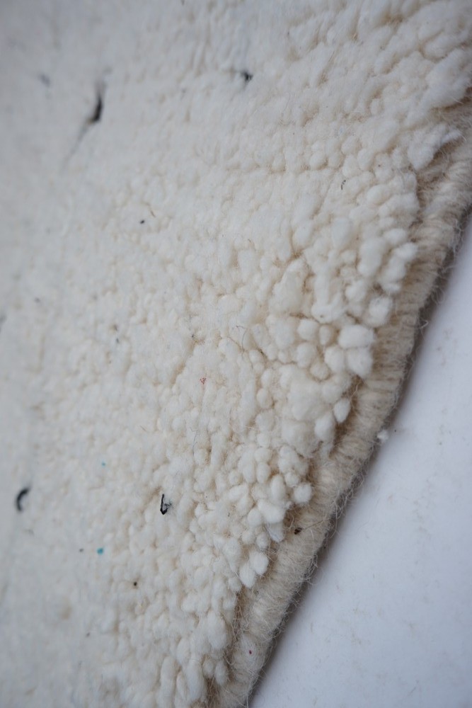 Tapis berbère en laine au design minimaliste, couleur blanc cassé avec des motifs texturés et des touches de noir.