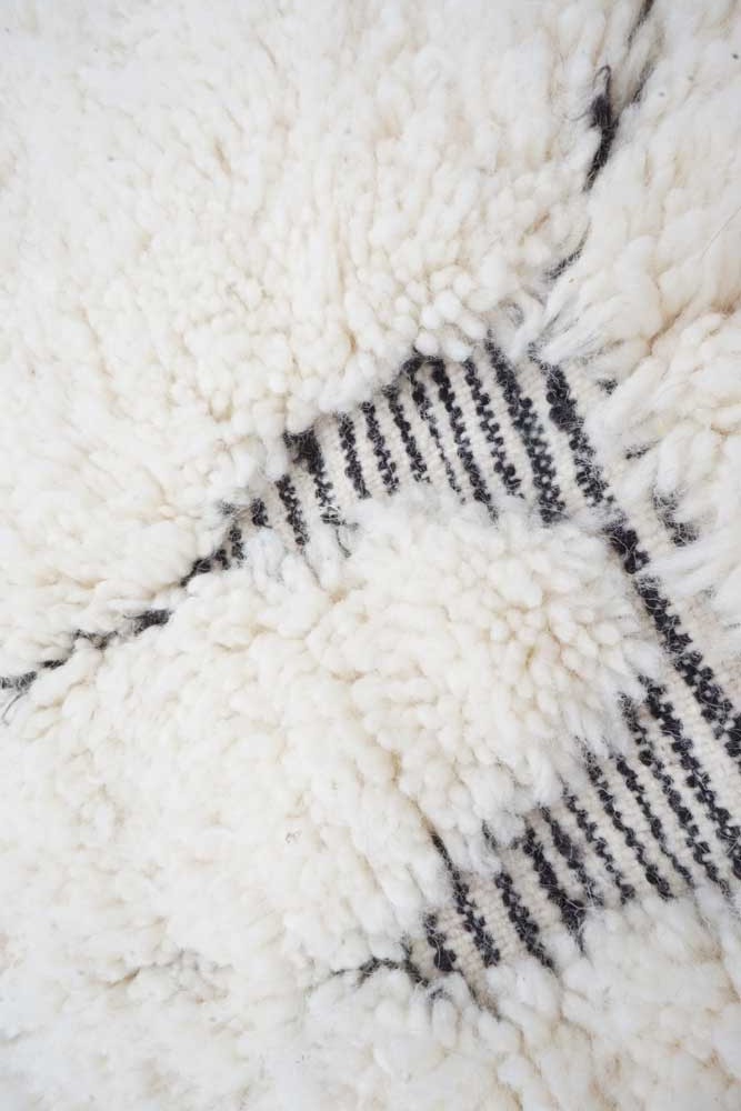 Tapis berbère blanc crémeux avec motifs géométriques en noir et texture en laine luxueuse.