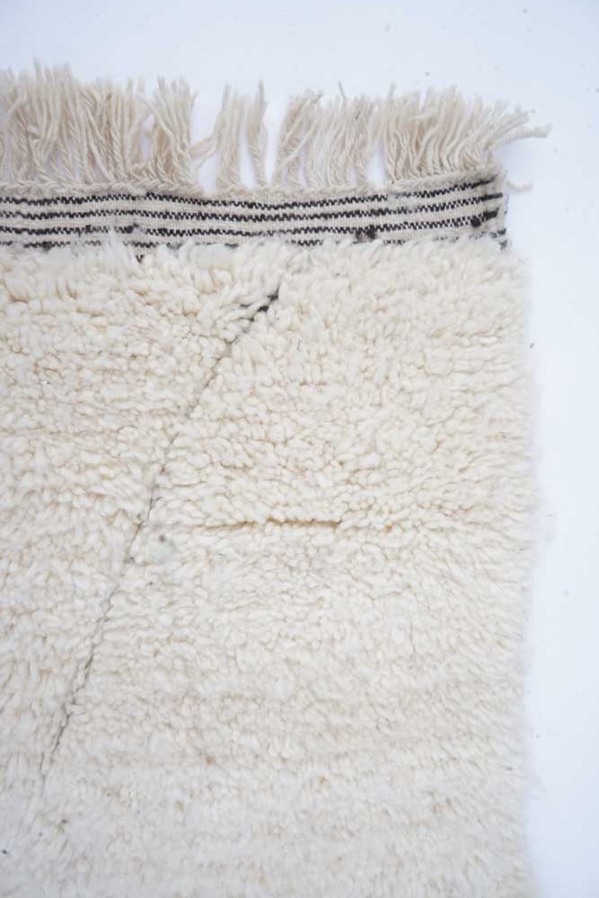 Tapis berbère en laine beige avec des motifs minimalistes et des franges noires, idéal pour un décor contemporain.
