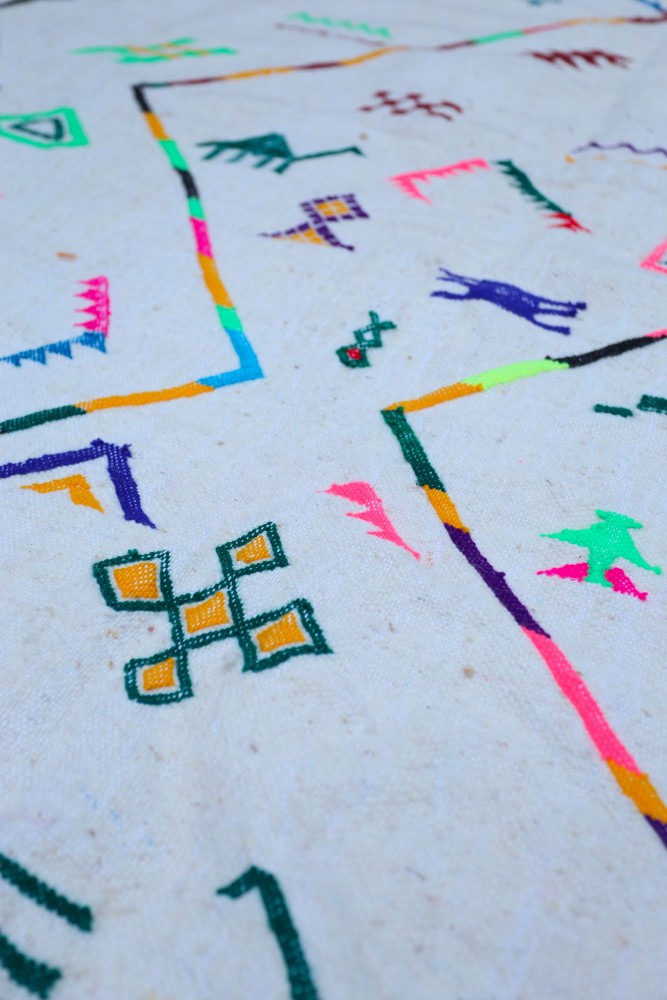 Tapis berbère coloré avec des motifs géométriques en rose, vert et jaune sur un fond crème.