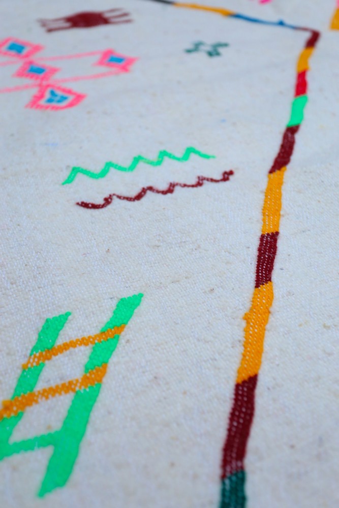 Tapis berbère coloré avec motifs géométriques en vert, rose et marron sur fond beige.