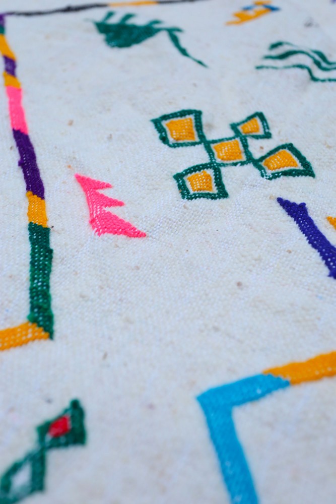Tapis berbère avec motifs colorés en jaune, vert et rose sur un fond beige, apportant une touche artisanale à votre intérieur.
