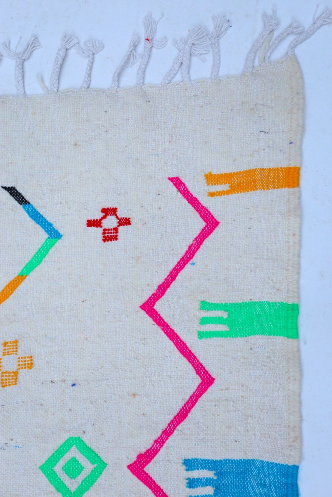 Tapis berbère aux motifs géométriques colorés en rose, bleu, vert et orange sur fond crème.