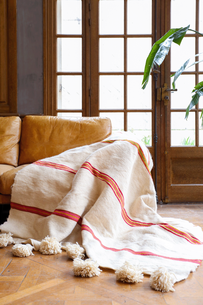 Manta bereber con borlas blancas y rayas rosas de lana, confeccionada a mano en Marruecos.