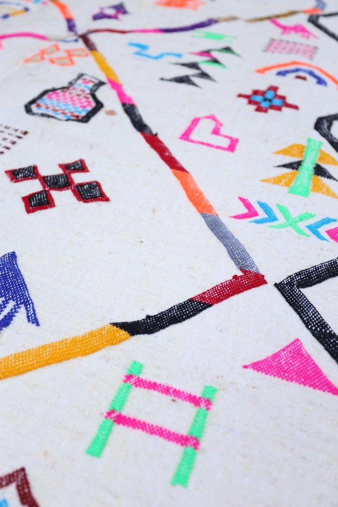 Tapis berbère aux motifs géométriques colorés, dominé par des teintes blanches, roses, vertes et noires.