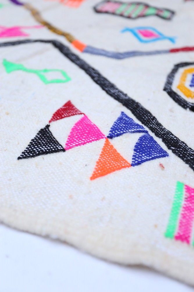Tapis berbère coloré avec motifs géométriques, dominé par des teintes vives comme le rose, le noir et le bleu.