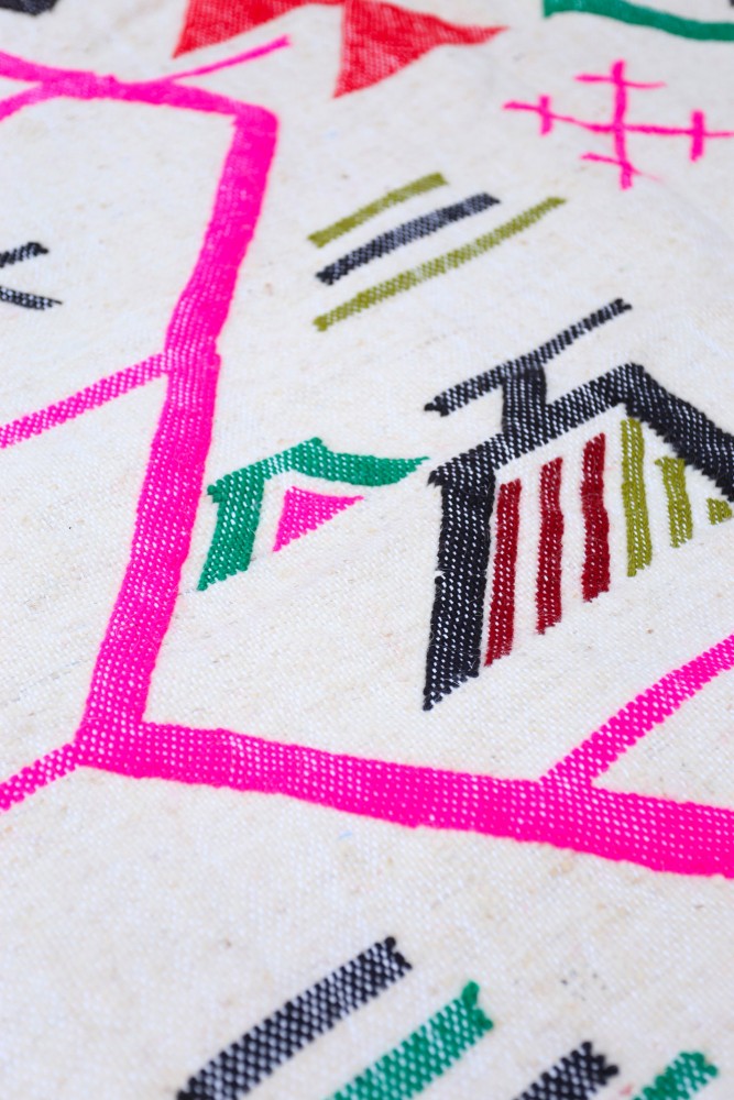 Tapis berbère coloré avec des motifs géométriques en rose, noir, vert et rouge sur un fond crème.