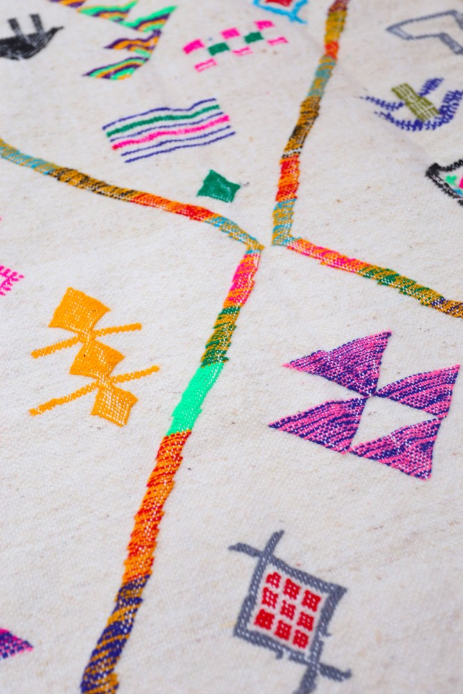 Tapis berbère avec motifs géométriques colorés sur fond beige, alliant tradition et modernité.