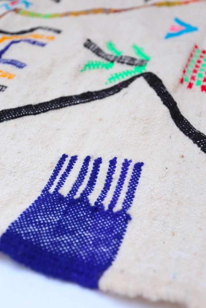 Tapis berbère à motifs géométriques colorés, dominé par des teintes beige, bleu et noir, ajoutant une touche artisanale.
