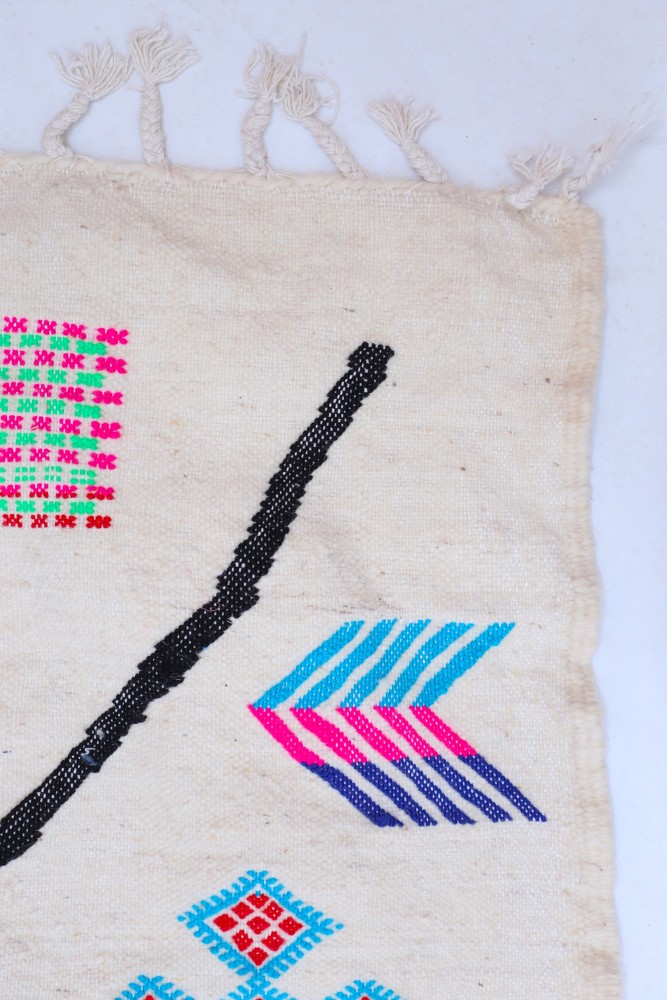 Tapis berbère aux motifs colorés, dominé par des teintes vives comme le rose, le bleu et le noir sur fond crème.