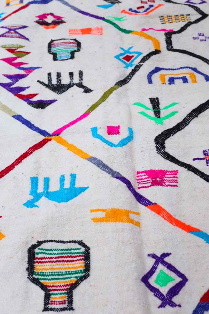 Tapis berbère coloré avec des motifs géométriques vifs sur un fond blanc, alliant tradition et modernité.