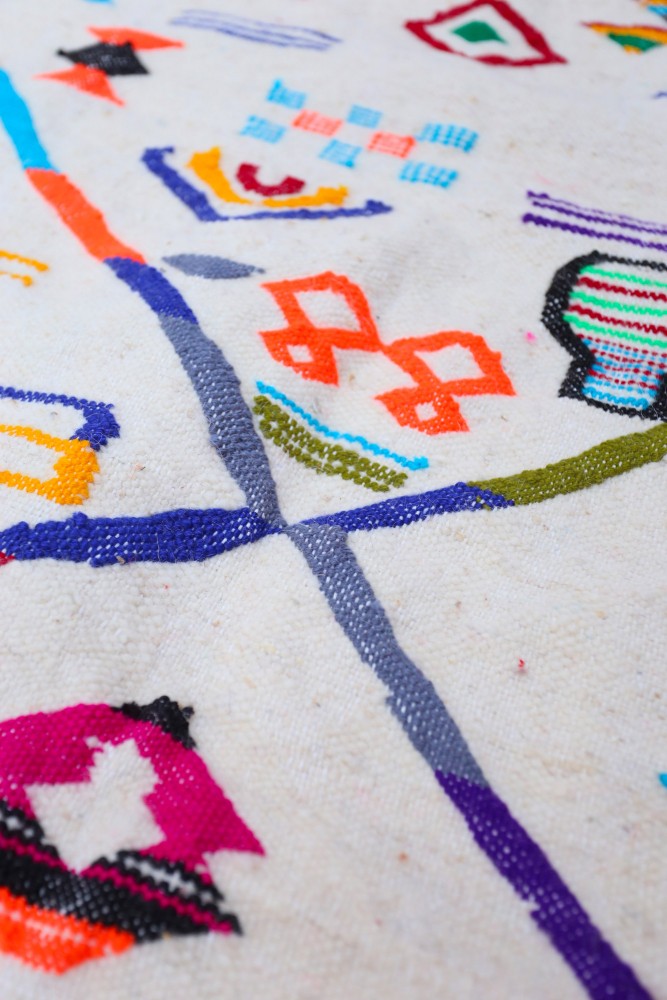 Tapis berbère coloré avec des motifs géométriques vifs sur fond crème, parfait pour un intérieur moderne et chaleureux.