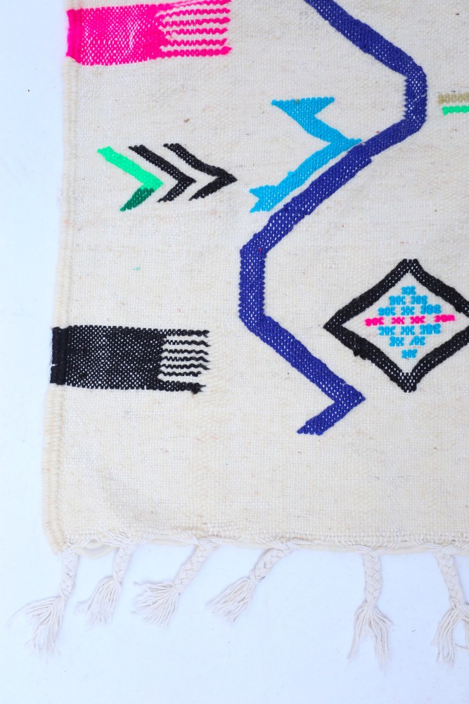 Tapis berbère aux motifs géométriques colorés, dominé par des teintes vives comme le rose, le bleu et le noir.