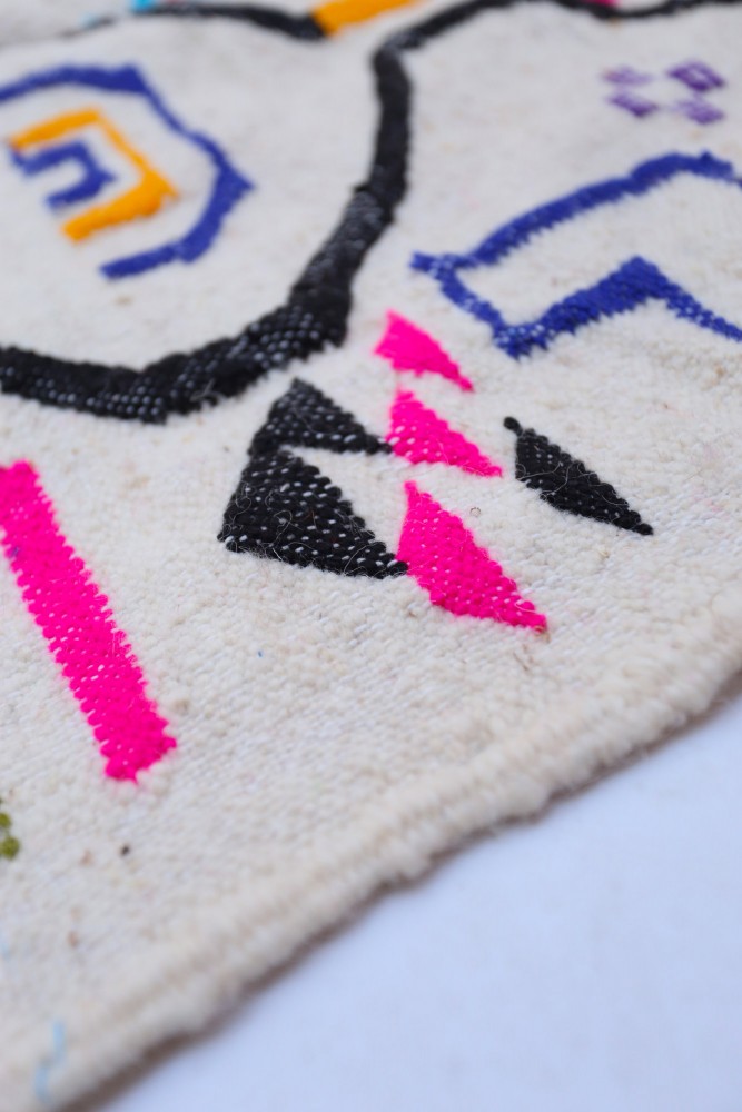 Tapis berbère aux motifs géométriques colorés en noir, rose, orange et bleu sur fond crème.