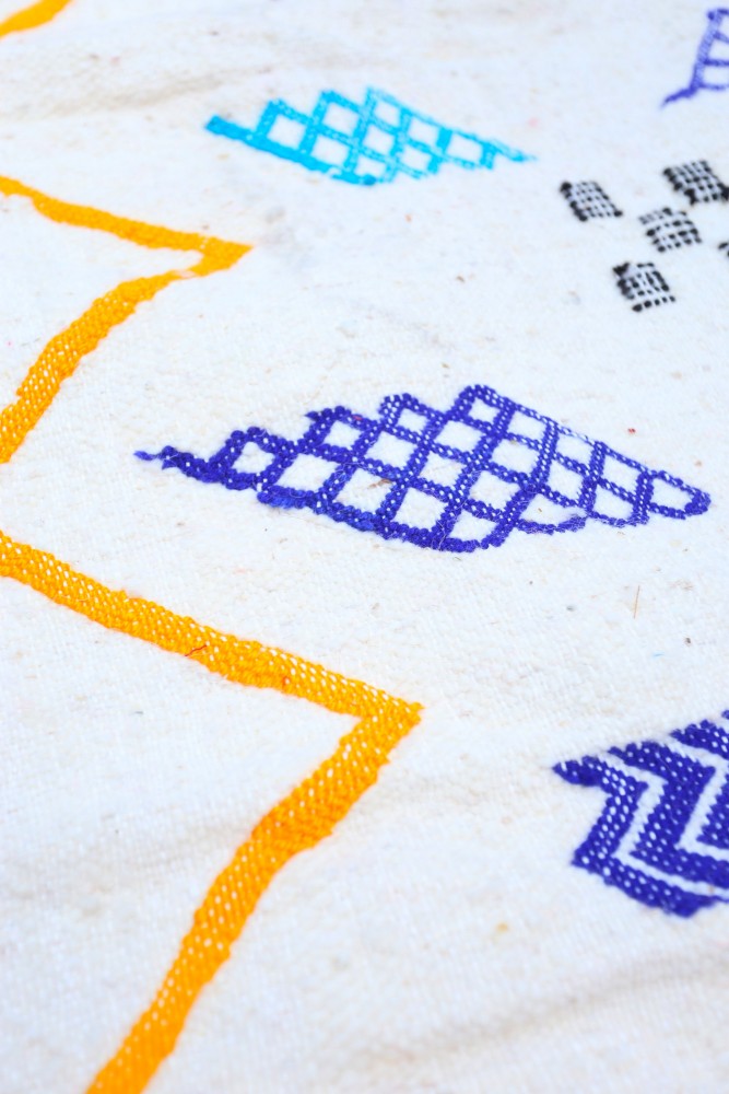 Tapis berbère aux motifs géométriques vibrants en bleu, violet et orange sur un fond beige.