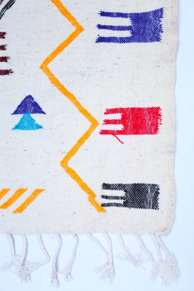 Tapis berbère coloré aux motifs géométriques avec des teintes vives tels que bleu, rouge et violet sur fond crème.