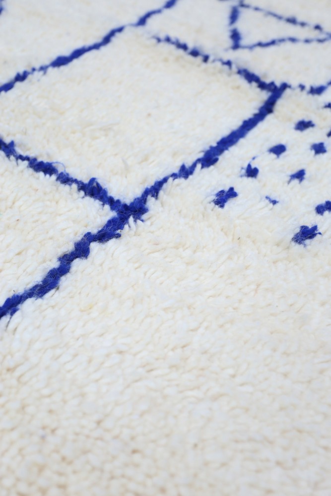 Tapis berbère à motifs géométriques bleus sur fond crème, alliant élégance et modernité.