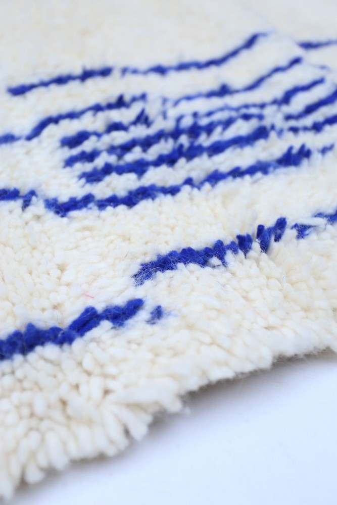Tapis berbère en laine avec un fond crème et des motifs bleus géométriques, ajoutant une touche artisanale à votre intérieur.