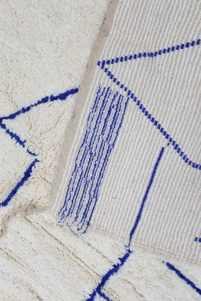Tapis berbère en écru avec motifs géométriques en bleu, idéal pour une décoration moderne et chaleureuse.