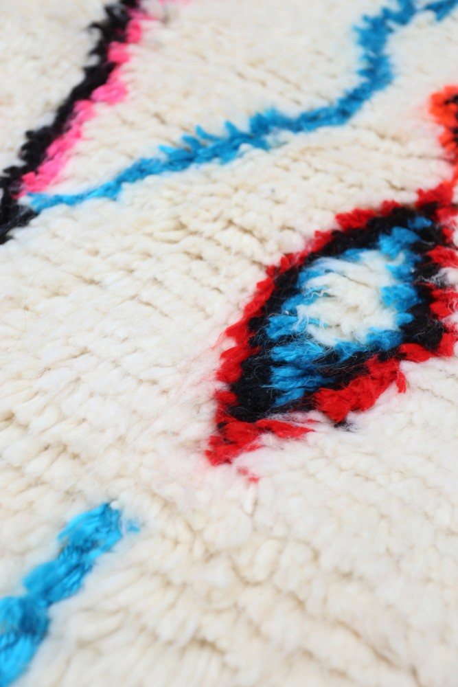 Tapis berbère blanc aux motifs géométriques colorés en bleu, rouge et noir.