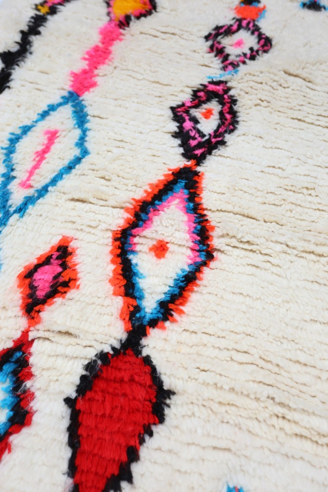 Tapis berbère aux motifs géométriques colorés sur fond crème, dominé par le rouge et le noir.