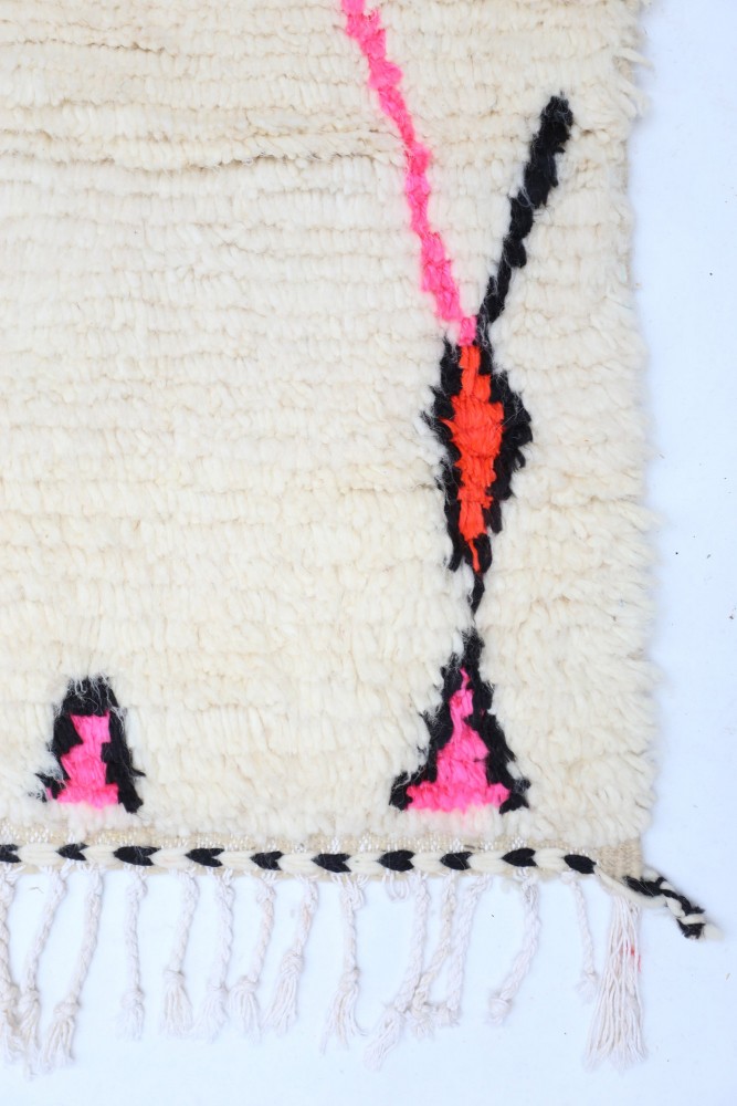 Tapis berbère blanc orné de motifs géométriques en noir, rose et orange.
