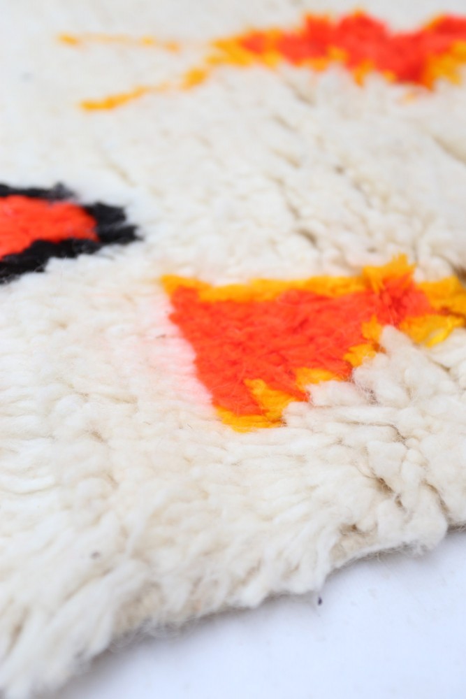 Tapis berbère en laine crème avec motifs géométriques en orange, noir et jaune.