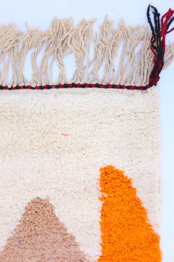Tapis berbère en laine avec des motifs géométriques en orange, beige et crème, idéal pour un intérieur chaleureux.