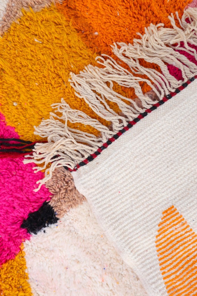 Tapis berbère aux motifs colorés avec des teintes vives de rose, orange et blanc, soulignant un design moderne et chaleureux.