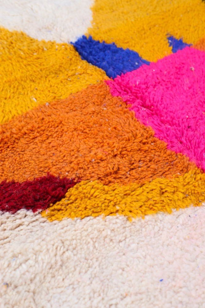 Tapis berbère coloré aux motifs géométriques, avec des tons vifs de rose, orange, bleu et beige.