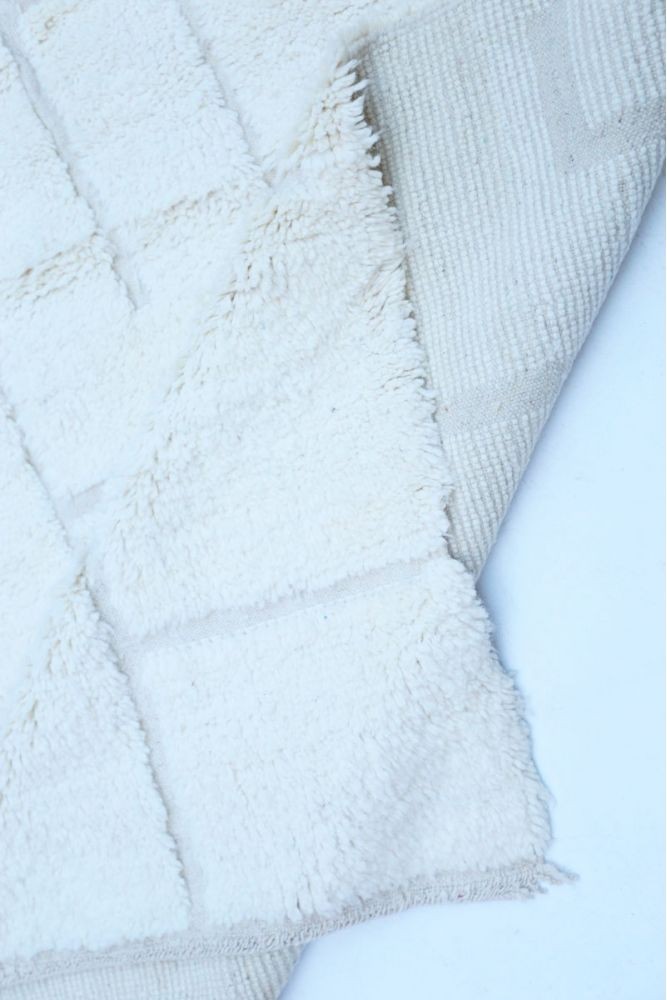 Tapis berbère en laine, blanc crémeux, motifs géométriques délicats et texturé.