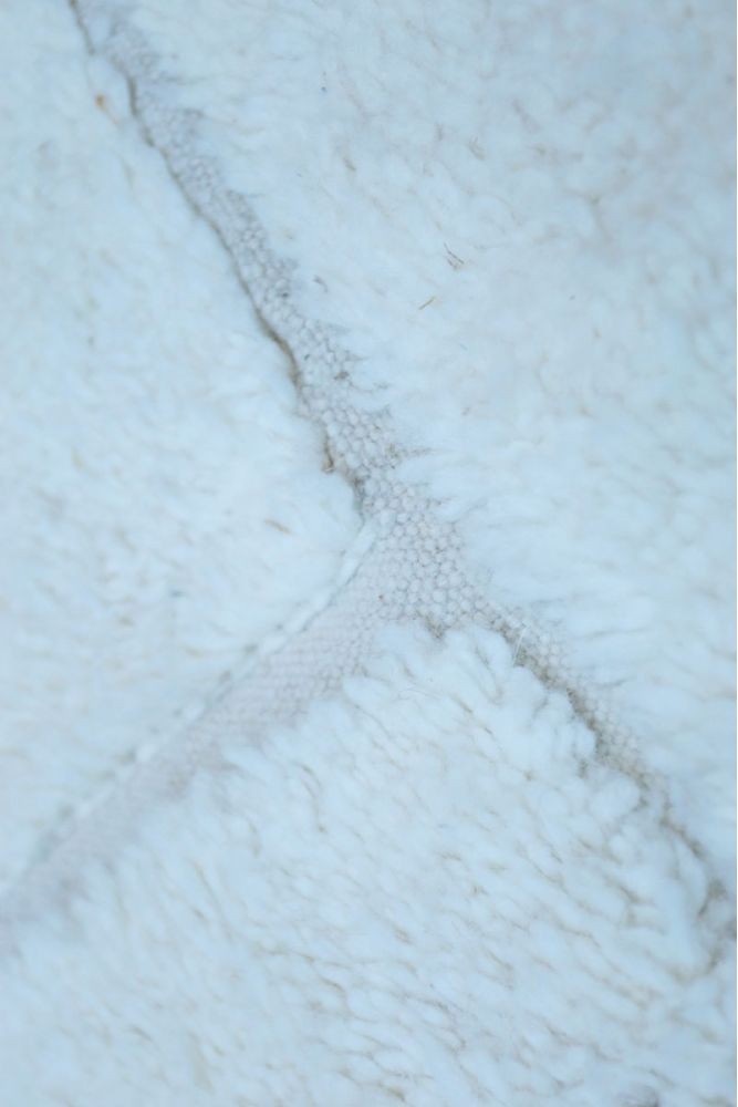 Tapis berbère blanc avec motifs géométriques doux et texture feutrée luxueuse.