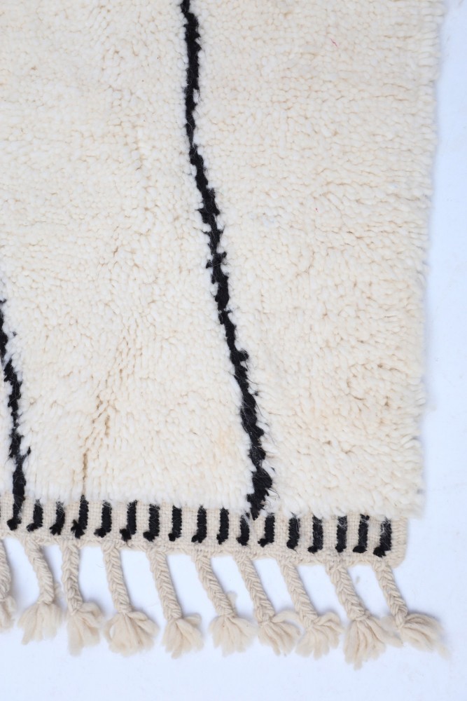 Tapis berbère au design minimaliste avec des motifs noirs sur fond beige et des franges élégantes.
