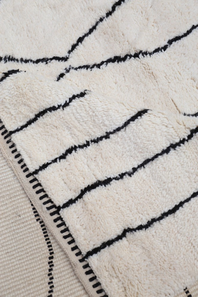 Tapis berbère en laine, avec des motifs linéaires noirs sur fond crème, ajoutant une touche moderne et chaleureuse.
