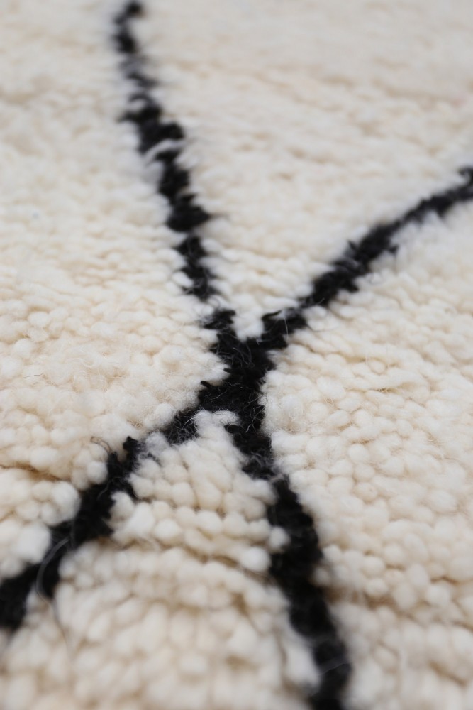 Tapis berbère en laine blanc crème avec motifs géométriques noirs en lignes contrastantes.