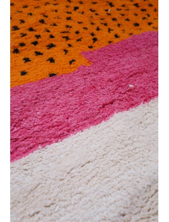 Tapis berb&egrave;re color&eacute; avec des motifs g&eacute;om&eacute;triques en orange, rose et cr&egrave;me, apportant une touche moderne et chaleureuse.