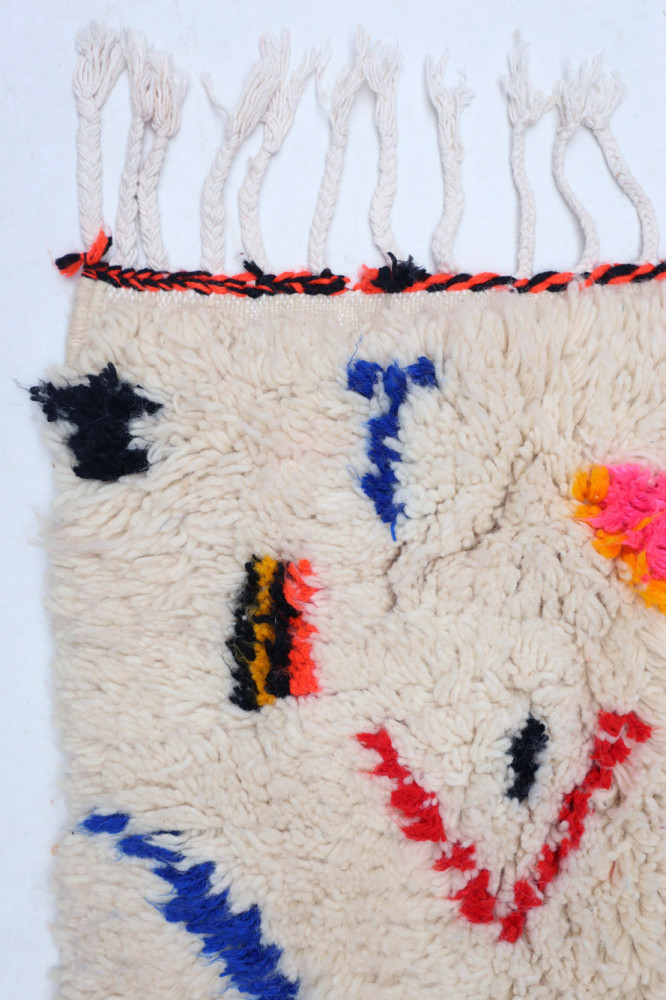 Tapis berbère contemporain avec des motifs colorés en noir, rouge et rose sur fond beige.