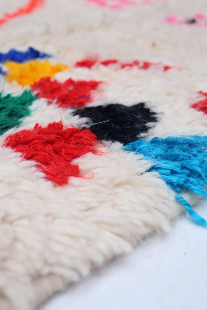 Tapis berbère en laine naturel avec motifs colorés rouge, bleu, noir et vert.