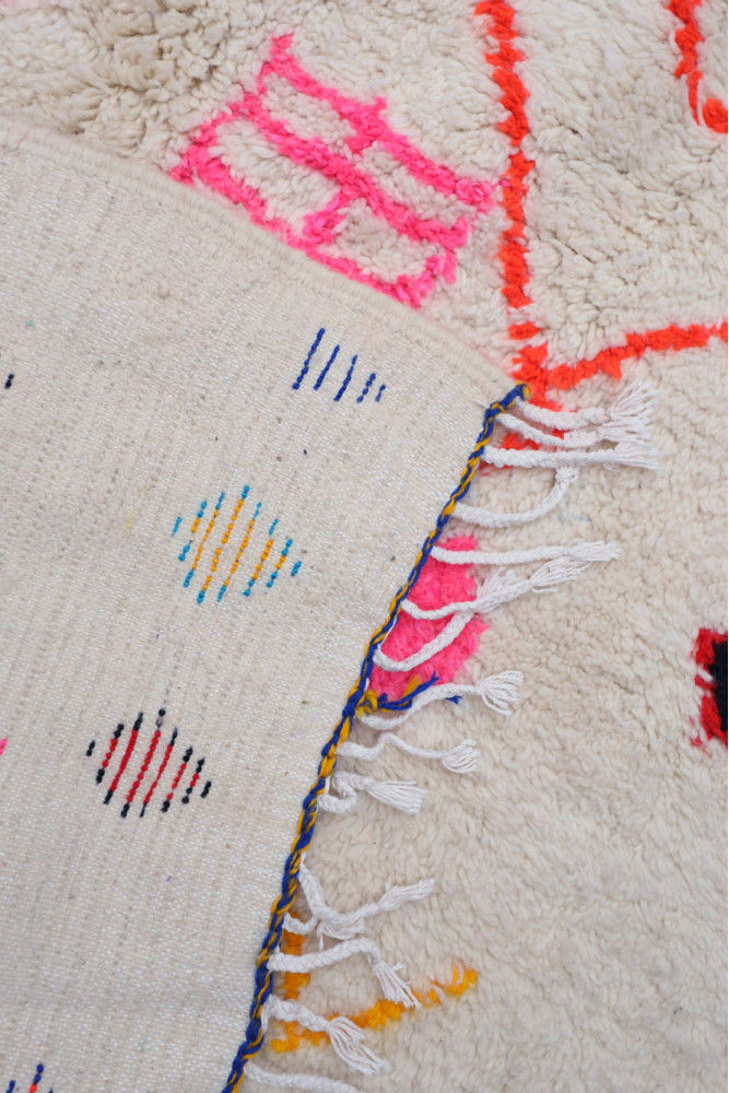 Tapis berbère à motifs géométriques colorés sur fond crème avec des franges.