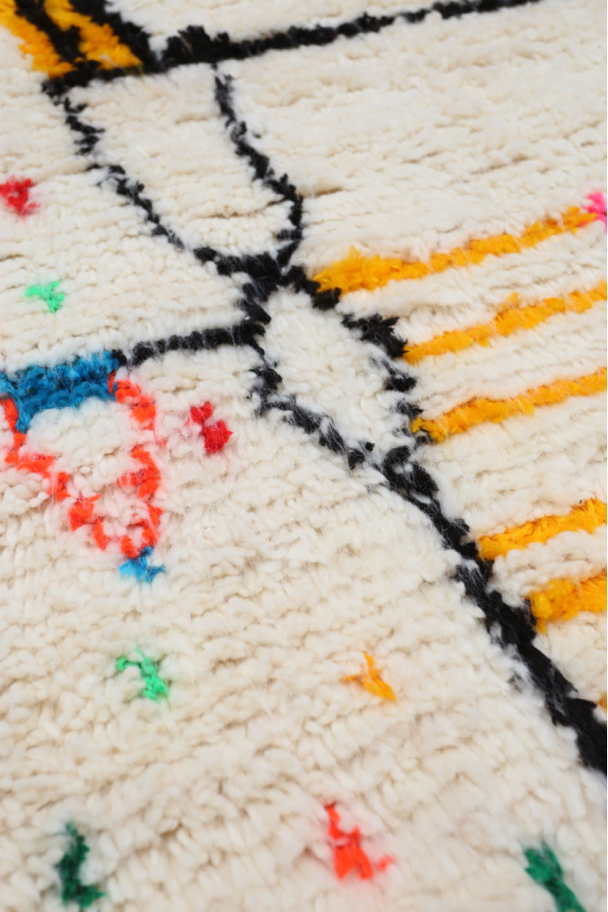 Tapis berbère aux motifs géométriques, couleurs vives et fond crème.