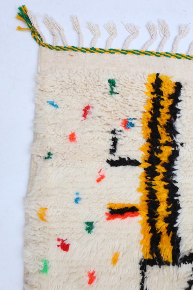 Tapis berbère en laine crémeux avec motifs géométriques noirs et éclats de couleurs vives.