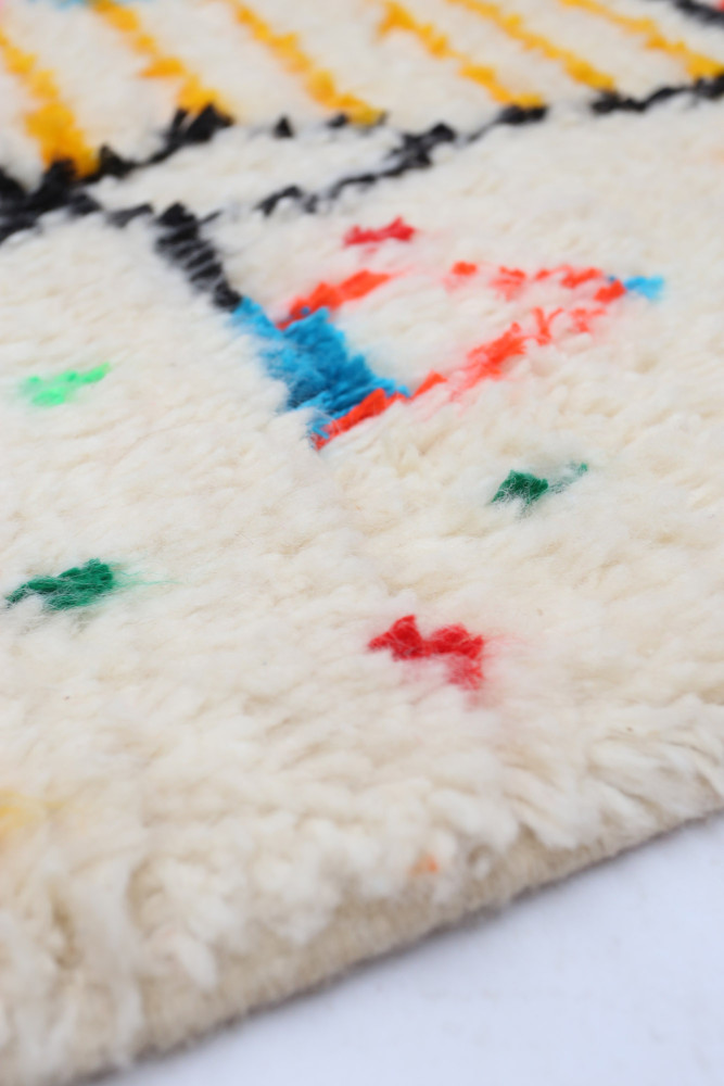 Tapis berbère au fond crème, motifs colorés avec des touches de rouge, bleu et noir.
