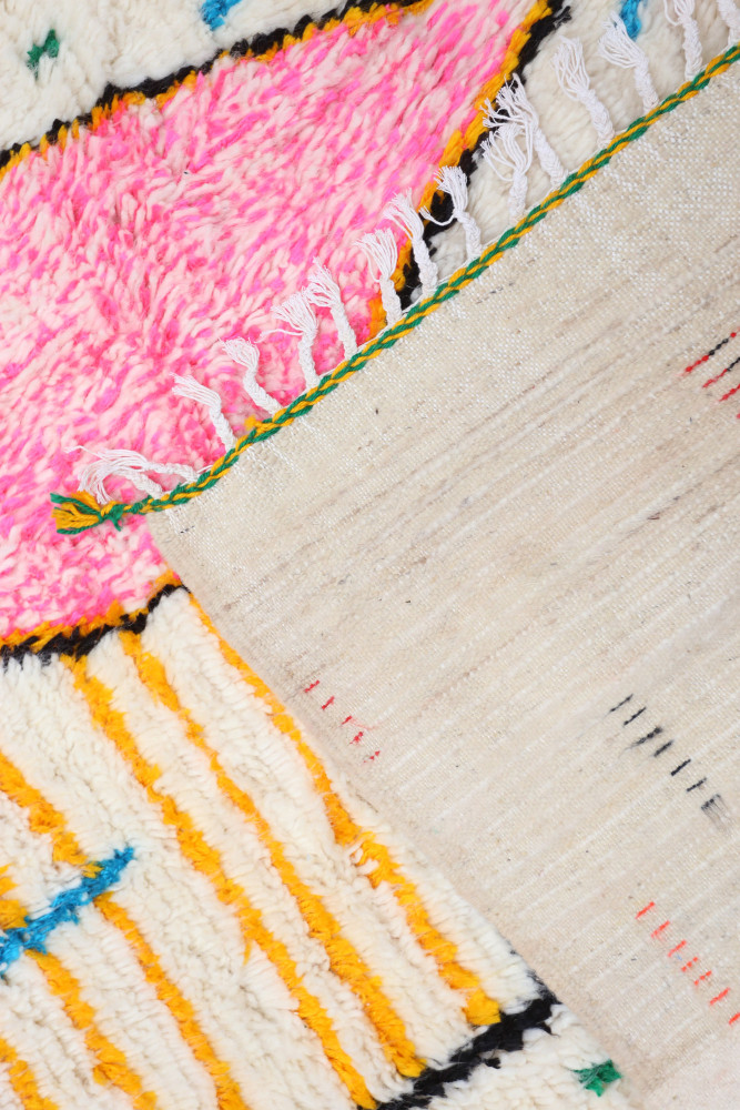 Tapis berbère coloré avec motifs géométriques en rose, jaune et noir.