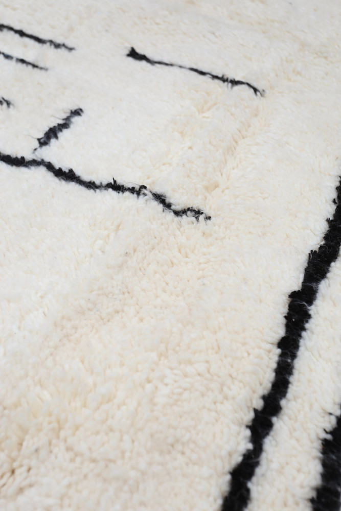 Tapis berbère moderne en laine, blanc crémeux avec des motifs géométriques noirs, ajoutant une touche élégante à tout intérieur.
