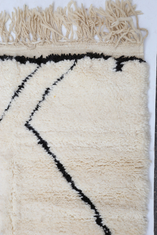 Tapis berbère en laine avec motifs noirs sur fond crème et franges élégantes pour une touche décorative chaleureuse.