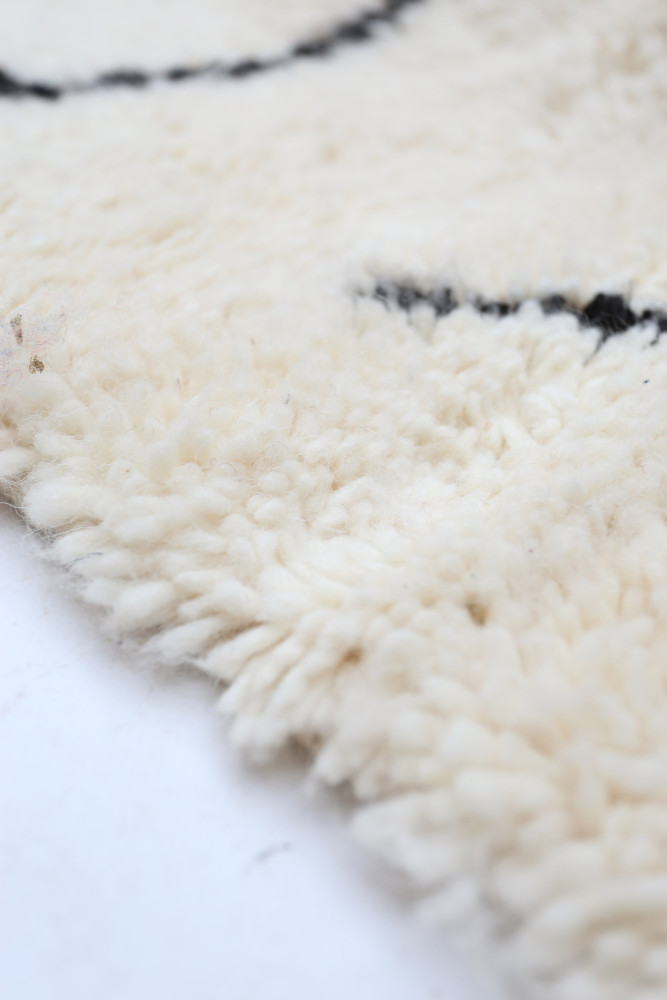 Tapis berbère en laine douce, couleur crème avec motifs noirs en forme de vagues, ajoutant une touche moderne et chaleureuse.