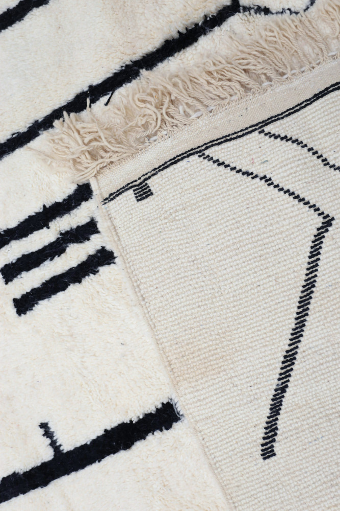 Tapis moderne en laine beige avec motifs géométriques en noir et franges, apportant une touche élégante à votre intérieur.