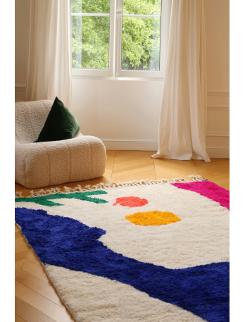 Tapis berb&egrave;re color&eacute; avec des motifs g&eacute;om&eacute;triques en bleu, rose, vert et orange sur fond cr&egrave;me.