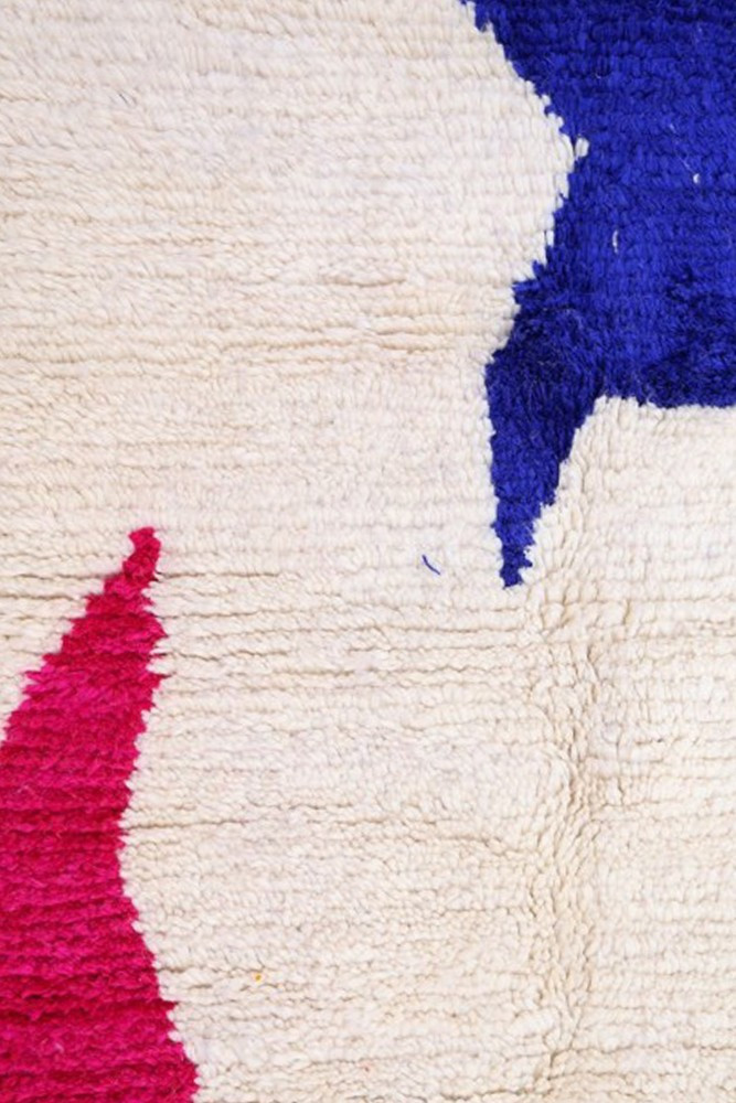 Tapis berbère au design contemporain avec des motifs abstraits en bleu, rose et beige sur fond clair.